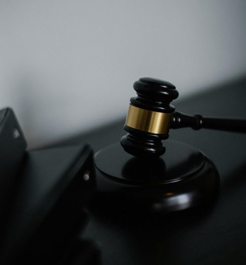 Black wooden gavel with golden strip on table near stack of folders in courthouse